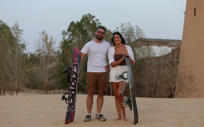 Couple standing with sandboarding board during Dubai desert safari